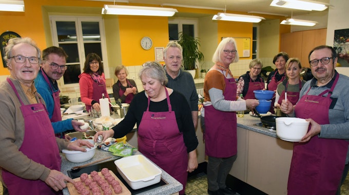 Mehrere Personen mit roten Schürzen stehen in einer großen Küche und sind Essen am Zubereiten.