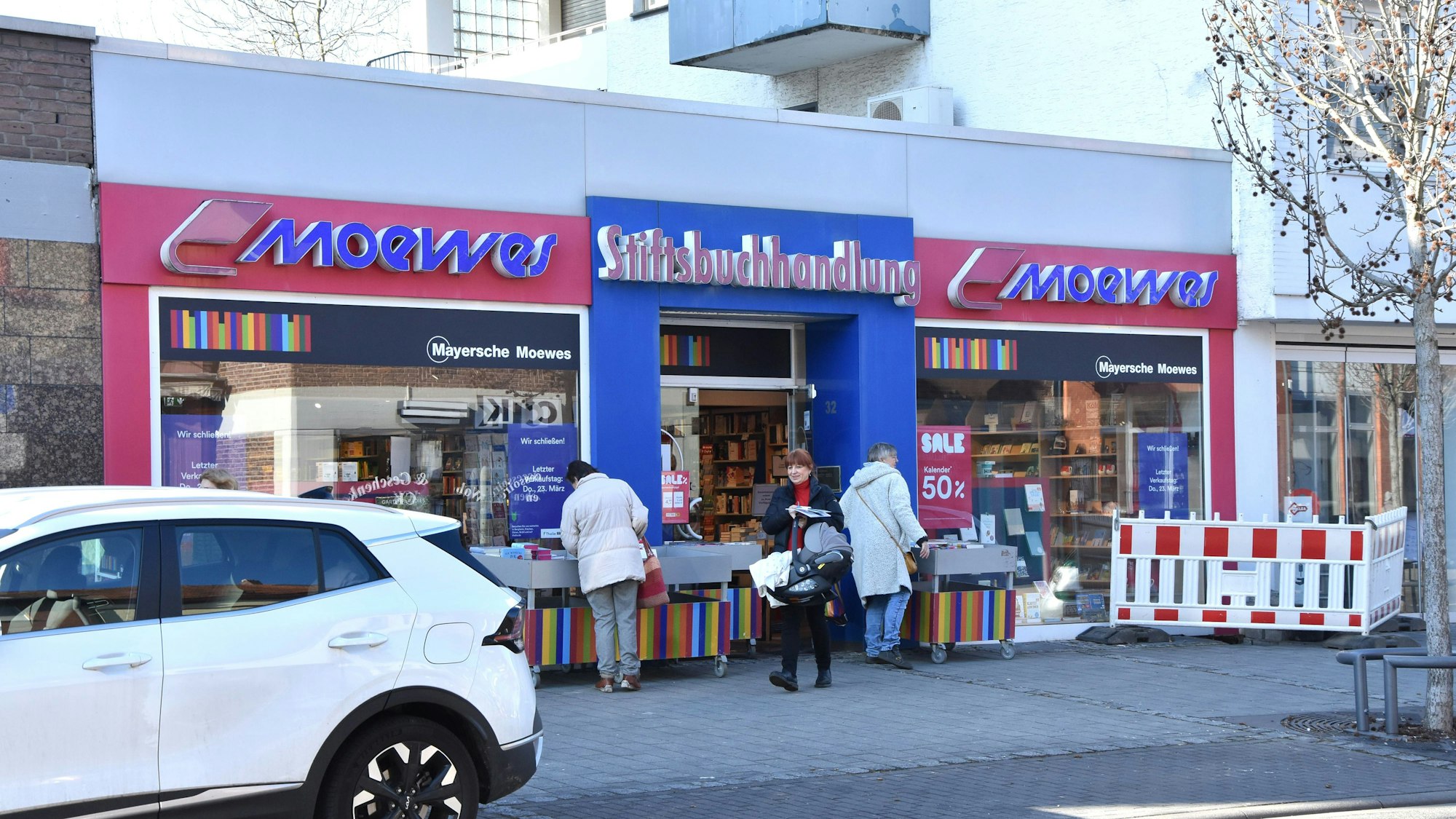 Das Foto zeigt die Stiftsbuchhandlung an der Hahnenstraße in Kerpen. Eine Kundin verlässt das Geschäft, zwei Frauen stöbern in Bücherkisten.