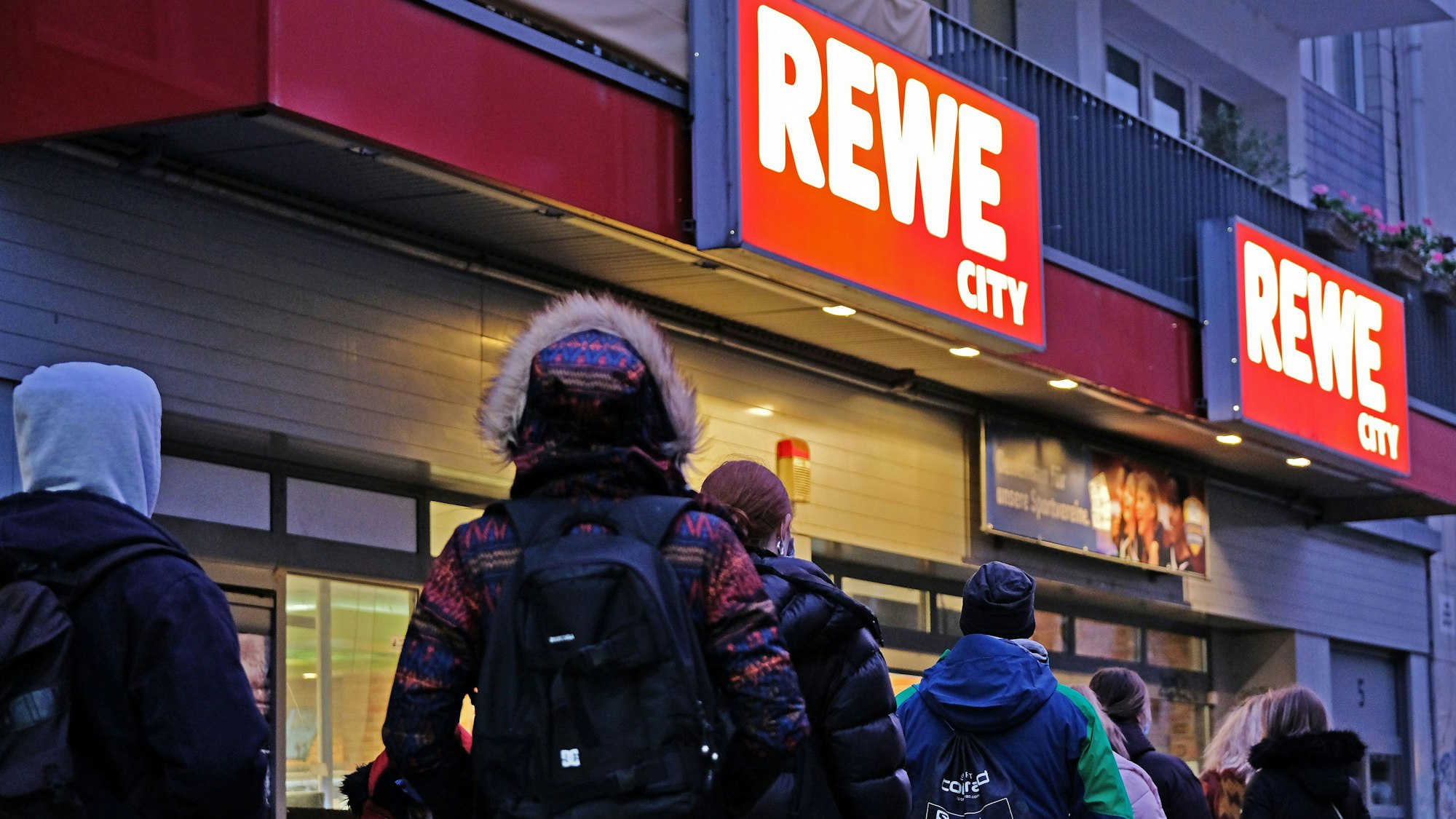 Menschen stehen vor einem Rewe-Supermarkt in Köln.