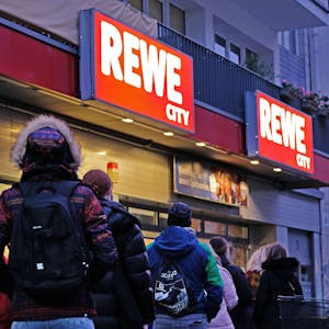 Menschen stehen vor einem Rewe-Supermarkt in Köln.