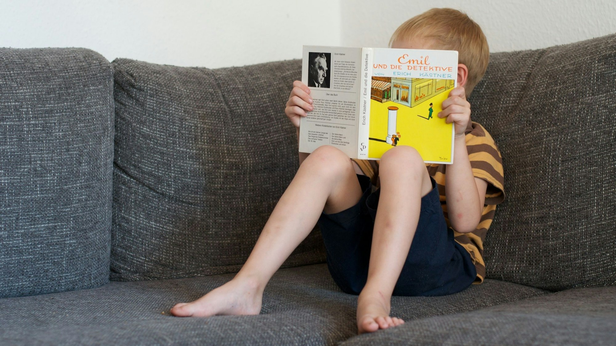 Ein Junge liest im Buch ‚Emil und die Detektive‘ von Erich Kästner.
