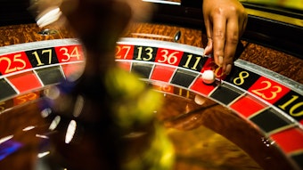 Eine Person greift mit der Hand beim Spiel Roulette nach einer Kugel, die auf Rot liegt.