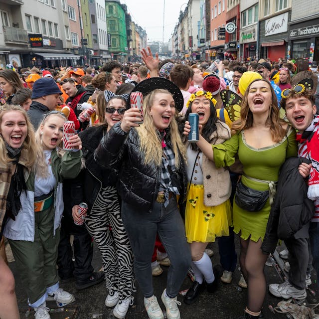 Eine Gruppe kostümierter Menschen feiert Karneval auf der Zülpicher Straße und lacht in die Kamera