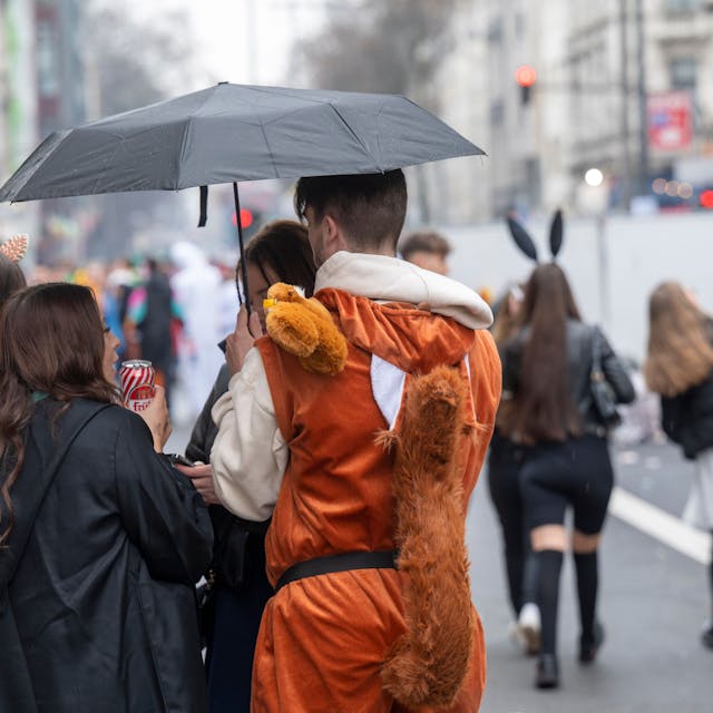 Ein Mann in einem Eichhörnchenkostüm und eine Frau im schwarzen Mantel stehen unter einem Regenschirm.