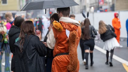 Ein Mann in einem Eichhörnchenkostüm und eine Frau im schwarzen Mantel stehen unter einem Regenschirm.