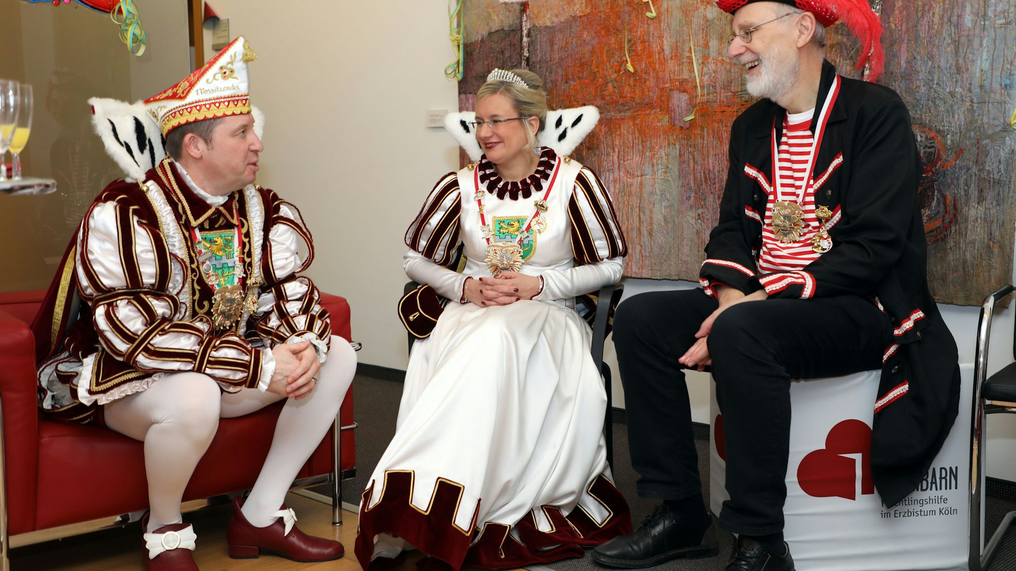 Weihbischof Ansgar Puff im Piratenkostüm sitzt mit Prinz Frank III. (Haag) und Jungfrau Melanie (Pfister) vom Bergisch Gladbacher Dreigestirn in einer Sitzecke und spricht.