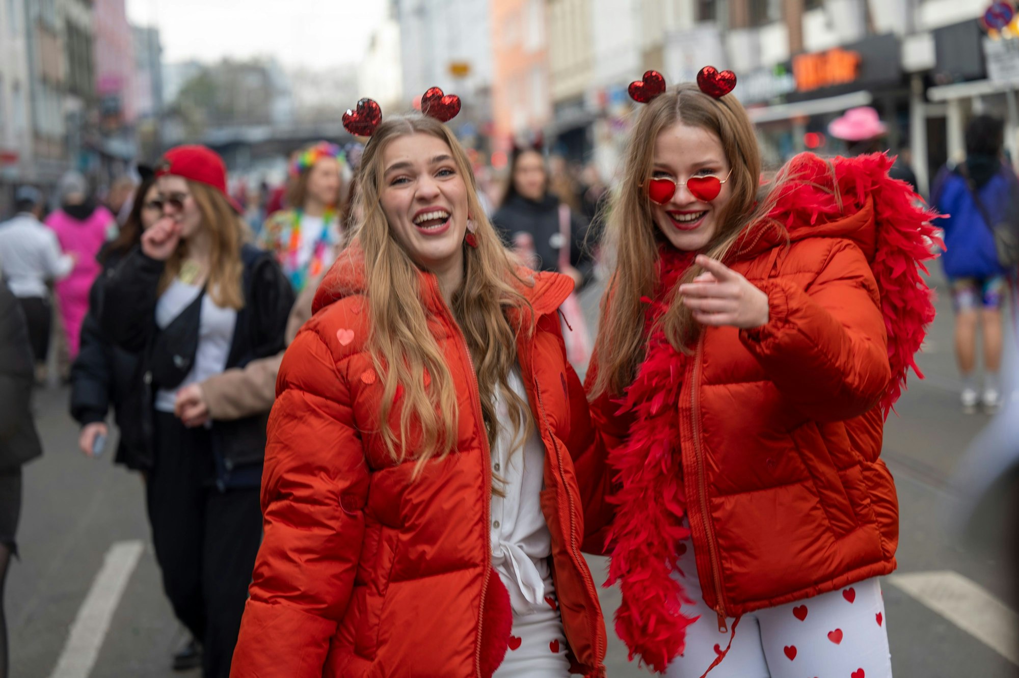 Zwei verkleidete Frauen mit Herzchen auf dem Haar und roten Daunenjacken stehen auf der Zülpicher Straße.
