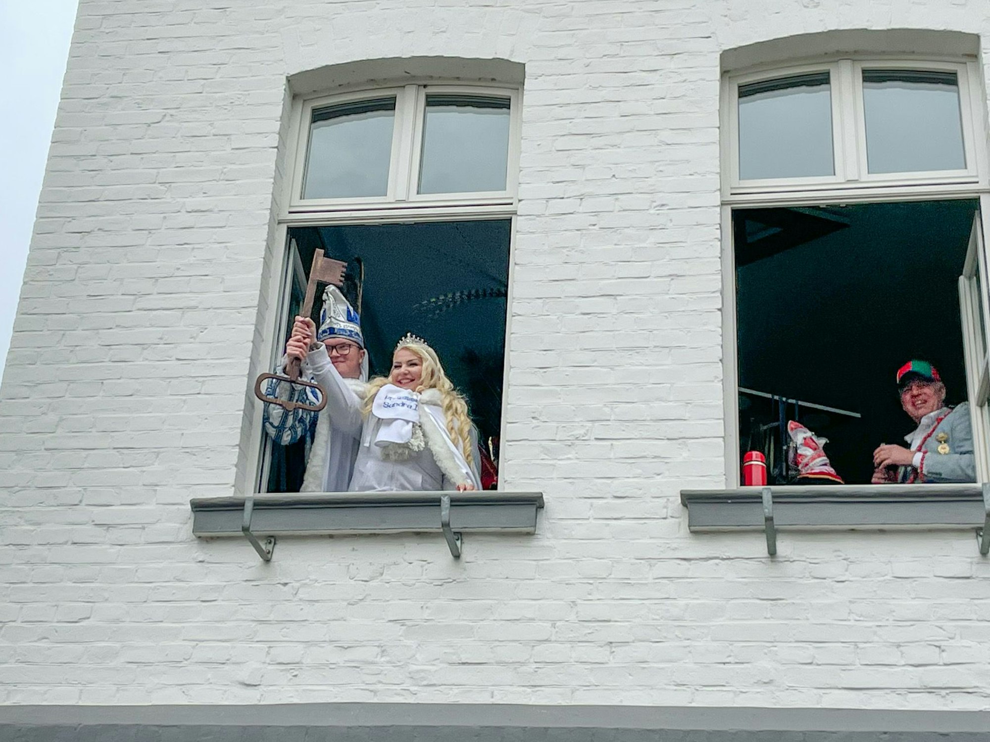 Marco I. und Sandra I. aus Blecher halten den Stadtschlüssel aus dem Rathausfenster. Bürgermeister Robert Lennerts steht an einem anderen Fenster und lächelt.