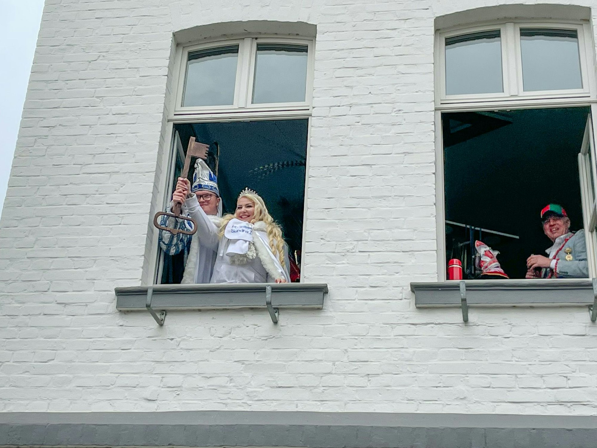 Marco I. und Sandra I. aus Blecher halten den Stadtschlüssel aus dem Rathausfenster. Bürgermeister Robert Lennerts steht an einem anderen Fenster und lächelt.