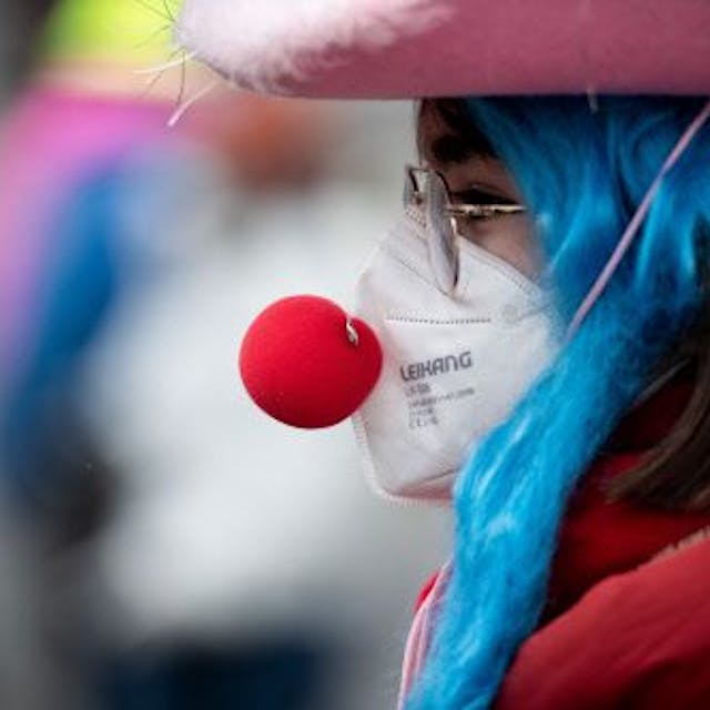 Eine verkleidete Frau trägt eine Clownsnase über einer FFP2 Maske.