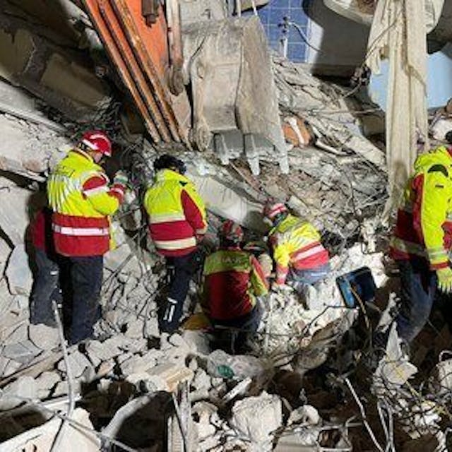 Fünf Retter in Warnanoraks suchen in Trümmern nach Überlebenden.