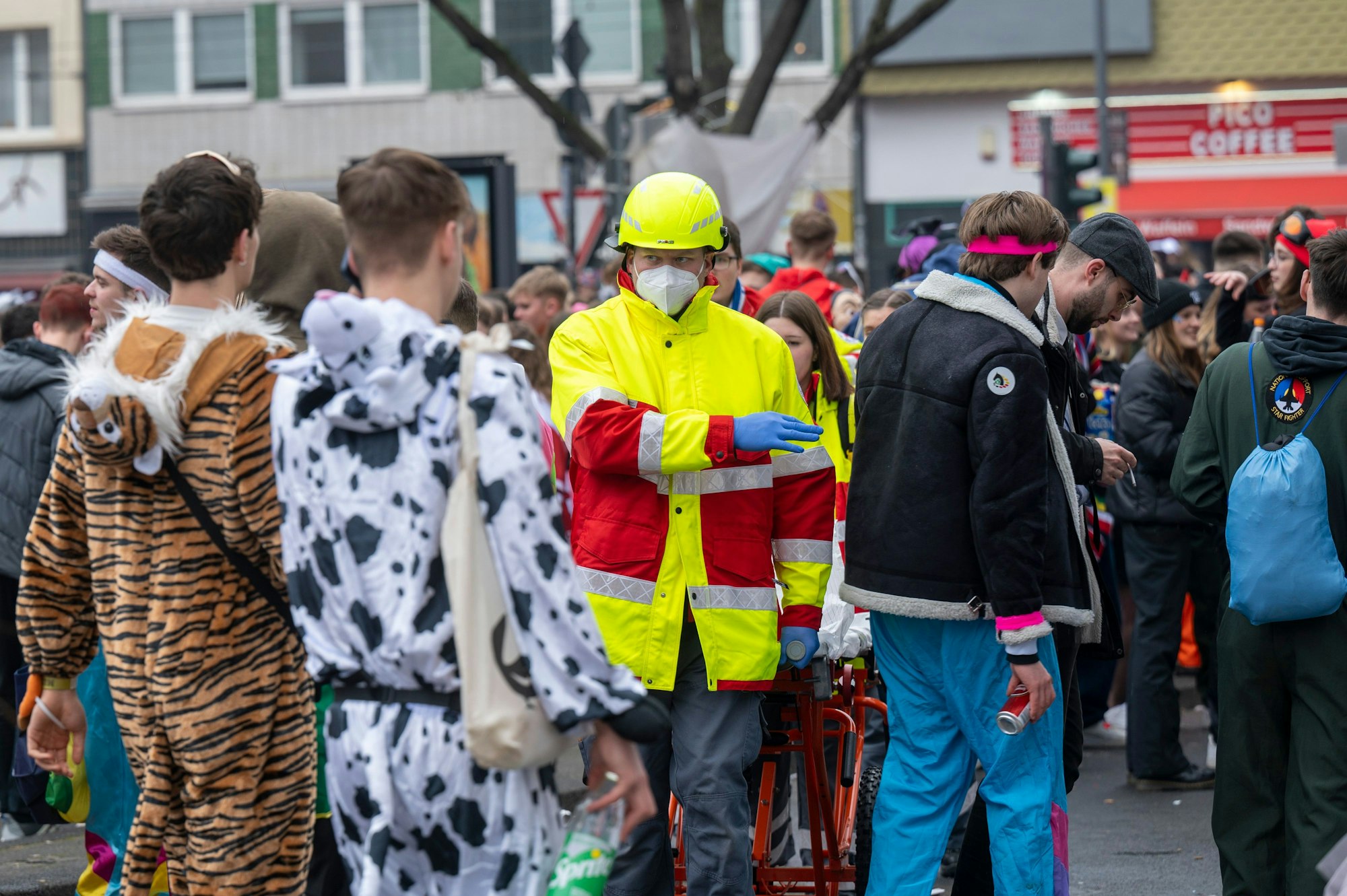 Ein Sanitäter in Warnbekleidung dirigiert einen Trupp durch die Menschenmenge auf der Straße.