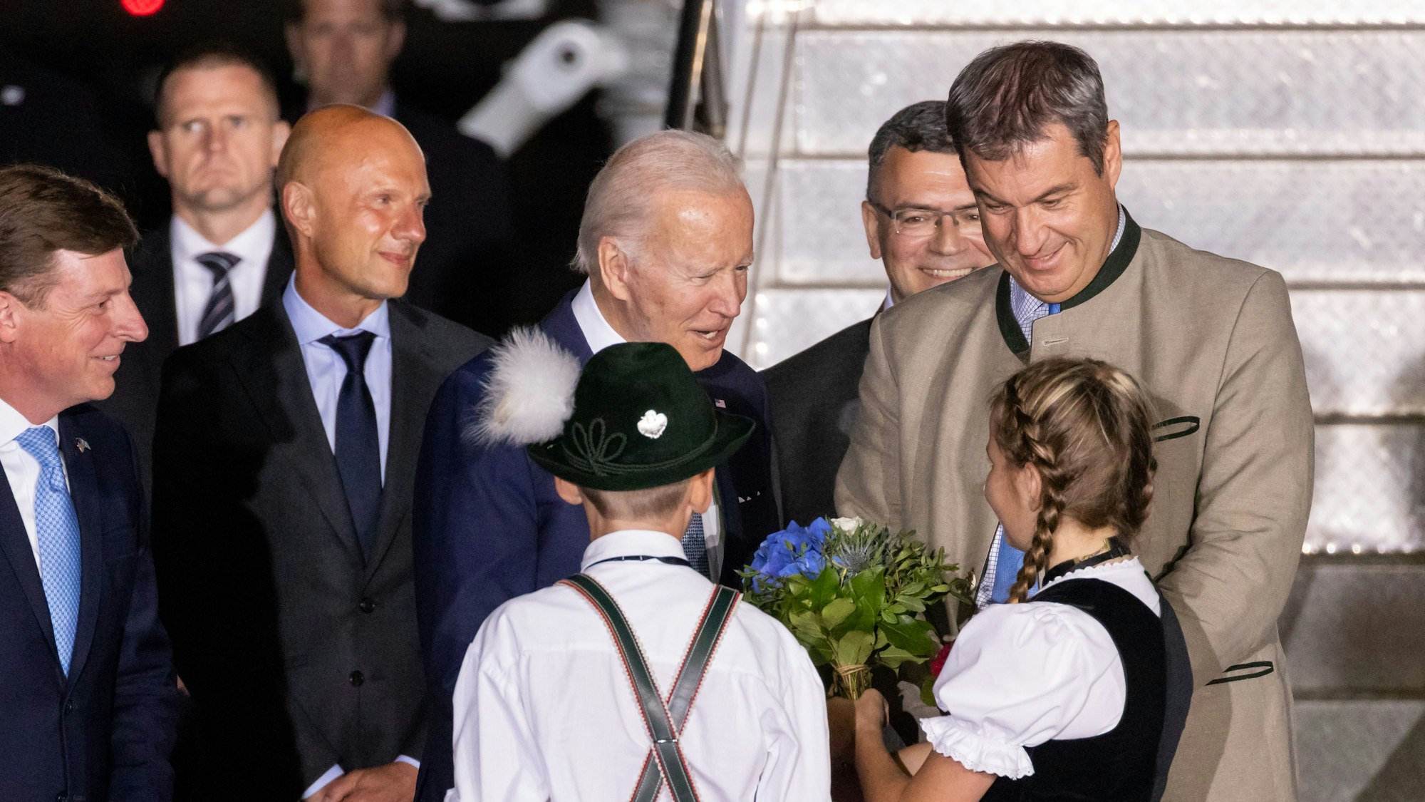 Zwei Kinder begrüßen Joe Biden (M.) am 25. Juni 2022 mit einem Blumenstrauß bei seiner Ankunft am Flughafen München.
