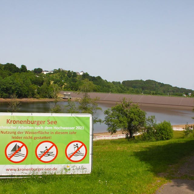Vor dem Kronenburger See steht ein großes Schild, auf dem steht: „Aufgrund technischer Arbeiten nach dem Hochwasser 2021 ist eine Nutzung der Wasserfläche in diesem Jahr leider nicht gestattet.“