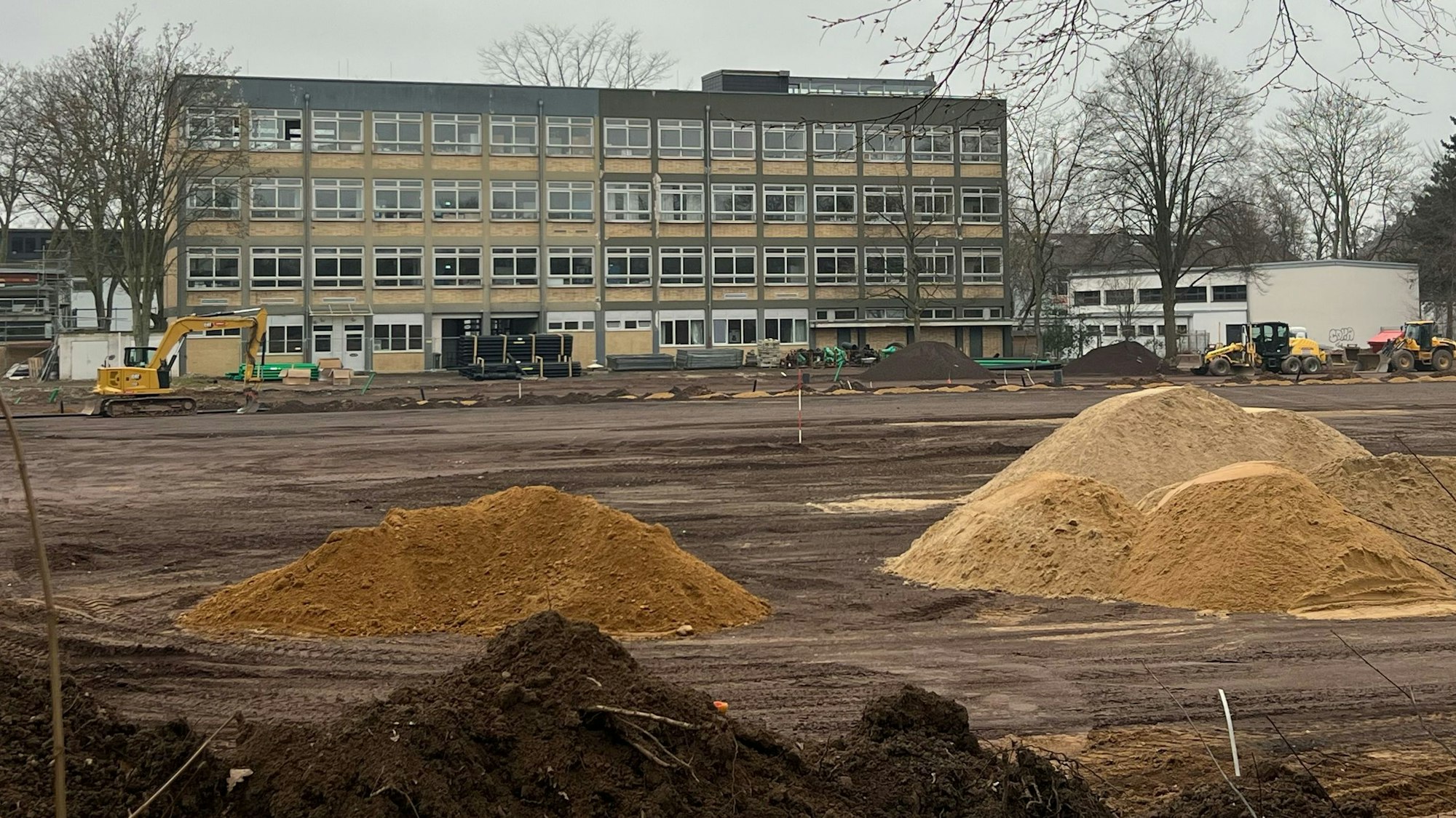 Das Bild zeigt aufgeschüttete Sandhaufen und Baugerät vor dem Gymnasium.