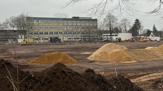 Das Bild zeigt aufgeschüttete Sandhaufen und Baugerät vor dem Gymnasium.