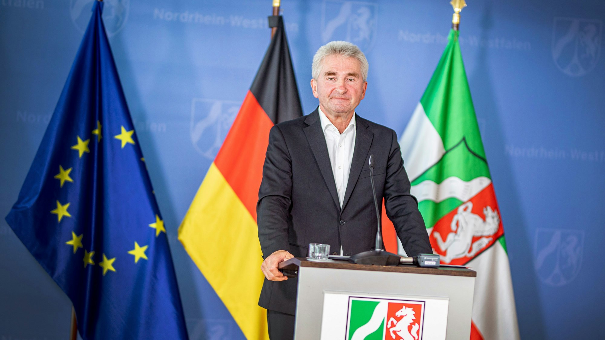 Andreas Pinkwart steht an einem Rednerpult mit dem Wappen Nordrhein-Westfalens. Hinter ihm steht eine Europa-, eine Deutschland- und eine NRW-Flagge.