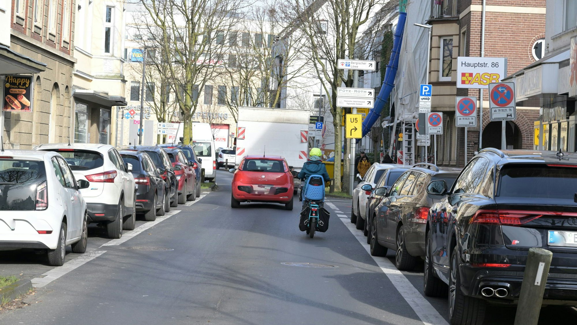 Ein Radfahrer und ein roter Wagen fahren auf der Unteren Hauptstraße in Bergisch Gladbach.