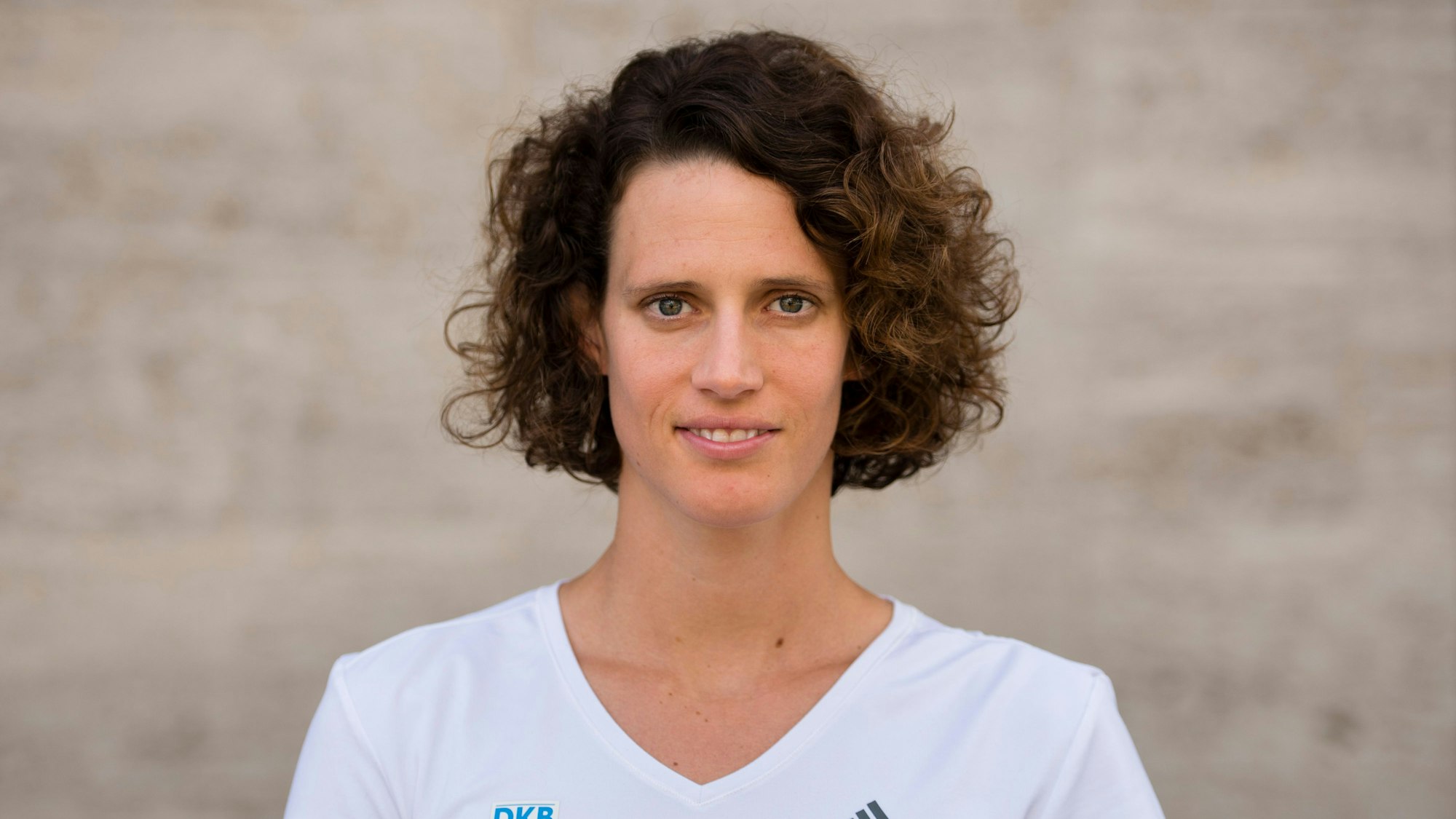 Lena Schöneborn steht mit einem weißen T-Shirt vor einer Wand.