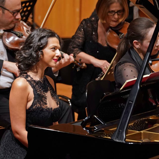 Pianistin Khatia Buniatishvili sitzt im Konzertsaal vor ihrem Flügel, sie hat dunkle Haare und trägt ein schwarzes Kleid.&nbsp;