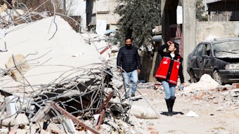 Eine Angehörige eines türkischen Rettungsdienstes und ein Mann gehen entlang von Trümmer, die durch das Erbeben ausgelöst wurden.