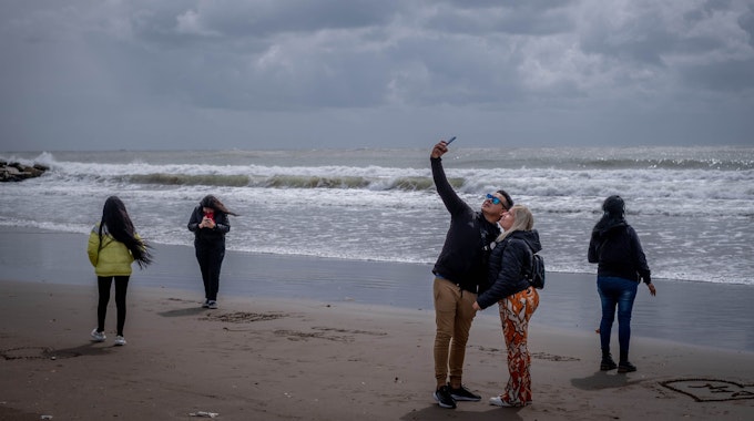 Menschen mit Jacken spazieren am Strand von Mar del Plata (Argentinien) und machen Selfies während des argentinischen Kälteeinbruchs mitten im Sommer.