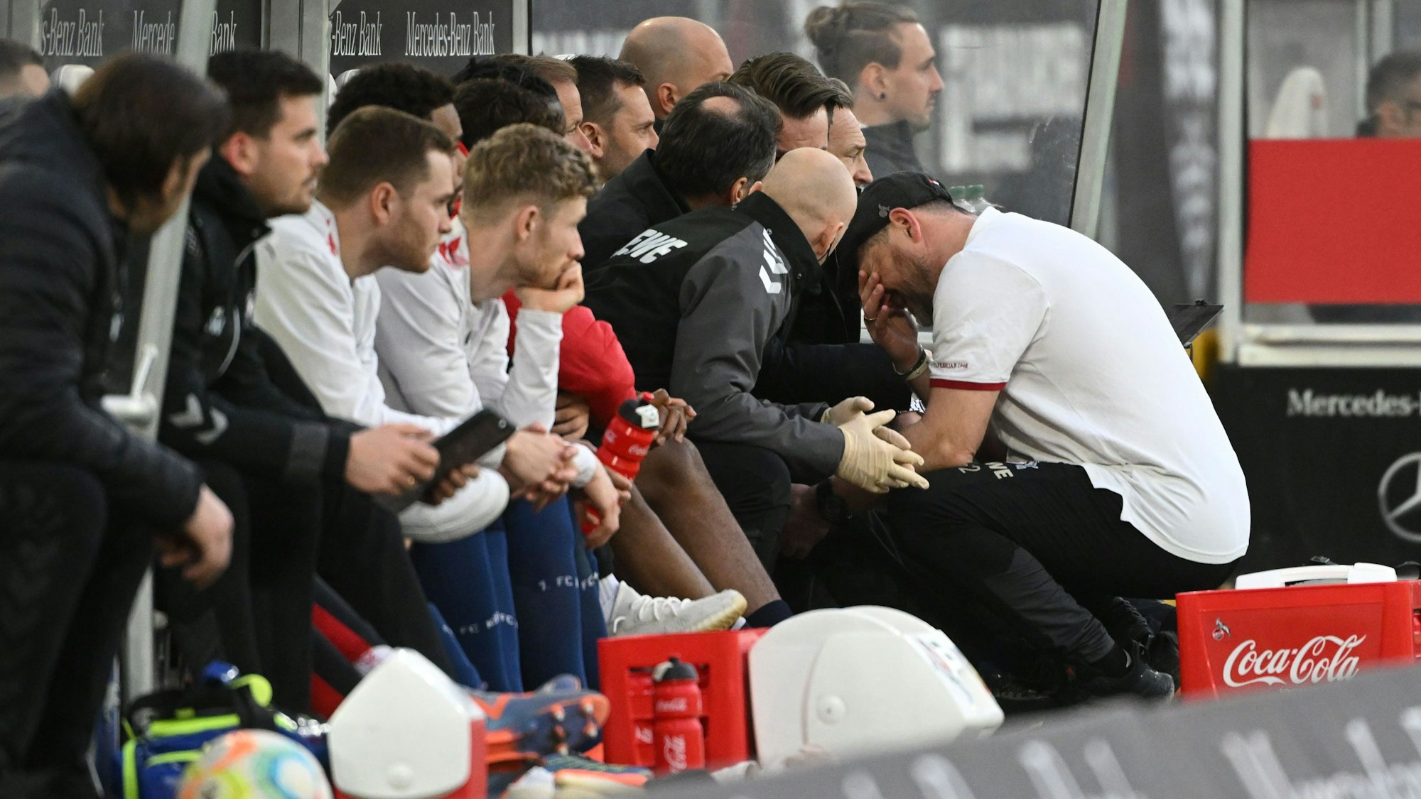Kölns Trainer Steffen Baumgart hockt an der Trainerbank und fasst sich ins Gesicht.