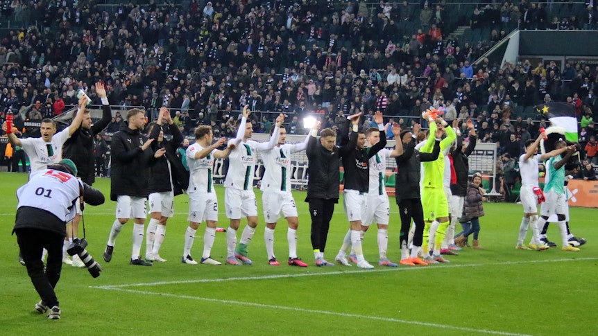 Die Mannschaft von Borussia Mönchengladbach feiert nach dem 3:2-Heimsieg gegen den FC Bayern München am 18. Februar 2023 mit den Fans im Borussia-Park. Die Spieler halten sich an den Händen und machen die La-Ola-Welle vor der Nordkurve.