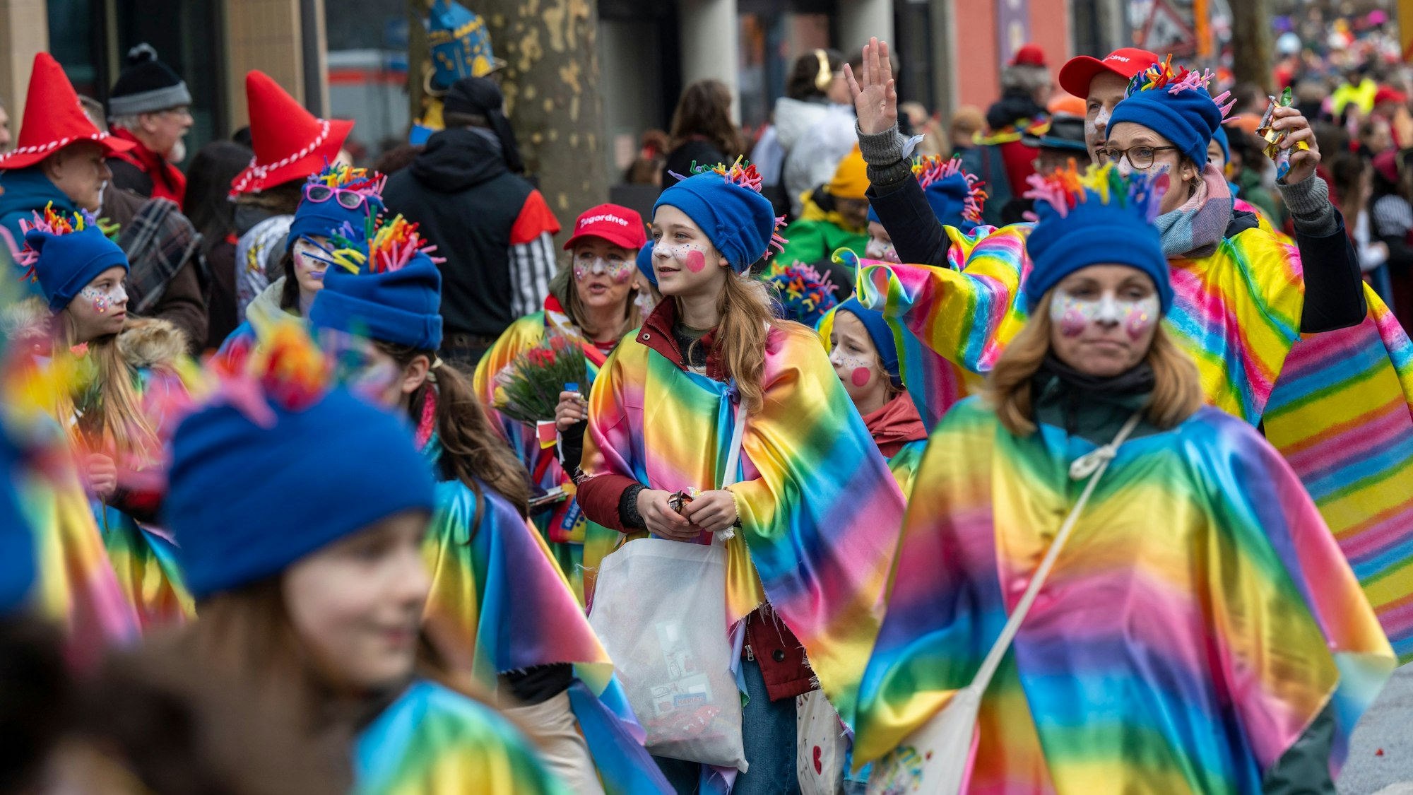 Teilnehmer der Schull- un Veedelszöch tragen Umhänge mit einem Regenbogenfarbenen Farbverlauf.