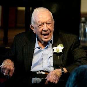 Ex-US-Präsident Jimmy Carter sitzt auf einem Stuhl und lächelt in die Kamera. Er trägt einen Anzug, in dessen Knopfloch eine Blume gesteckt ist.