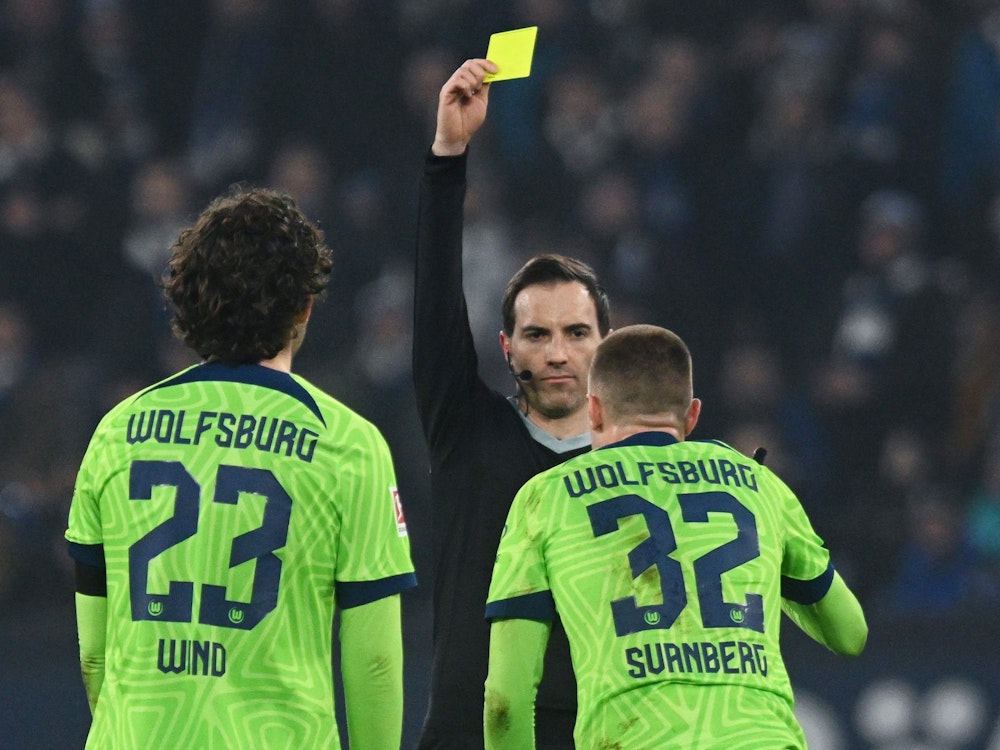 Schiedsrichter Benjamin Brand (M) zeigt Wolfsburgs Mattias Svanberg (2.vr) die Gelbe Karte.