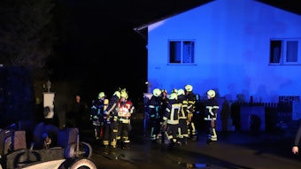 Feuerwehrleute stehen vor einem brennenden Haus.