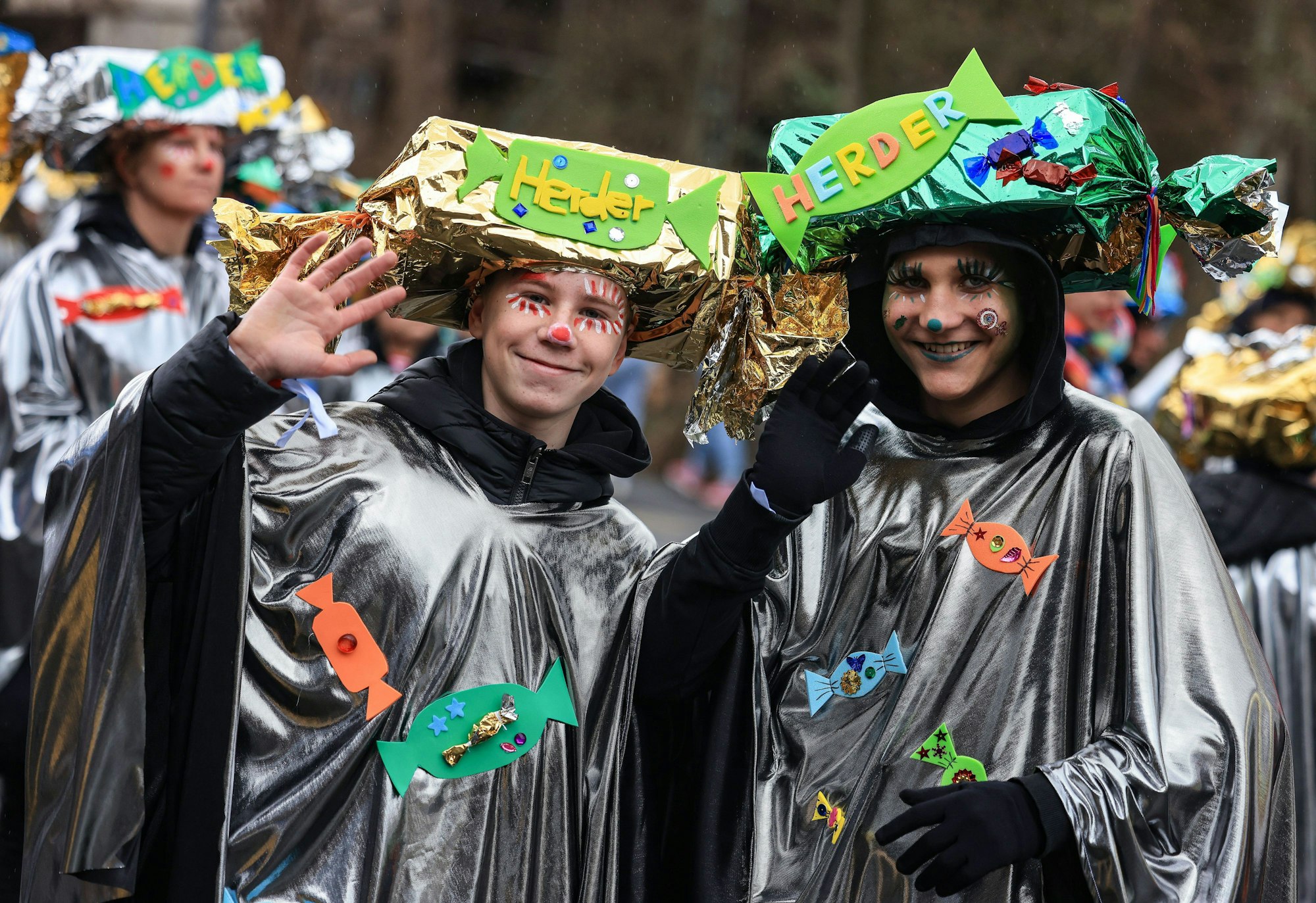 Zwei Schüler tragen silberfarbene, glänzende Umhänge und Hüte in Form von Bonbons.