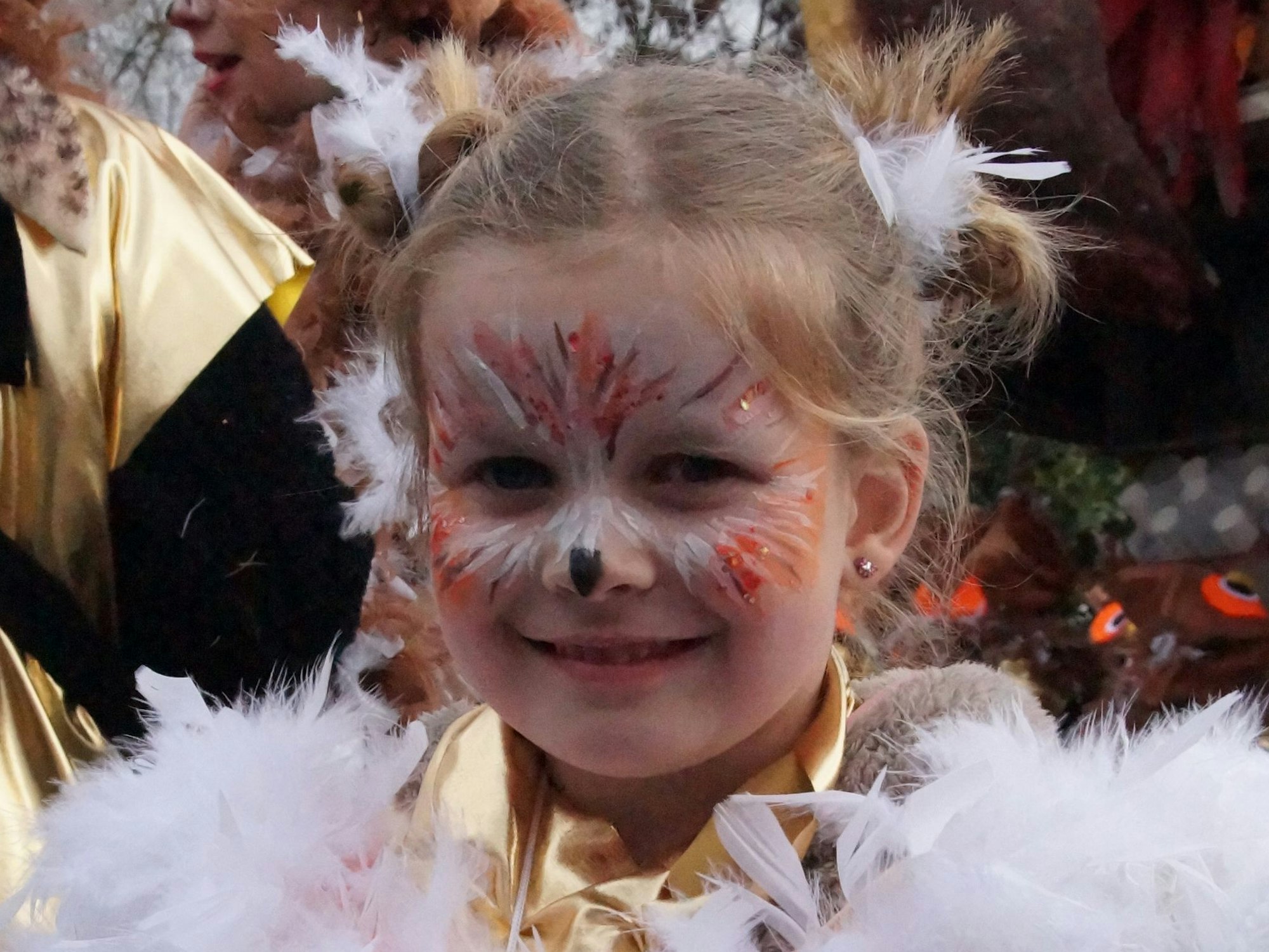 Porträt eines blonden Mädchens mit Eulen-Schminke im Gesicht und Federkragen um die Schultern.