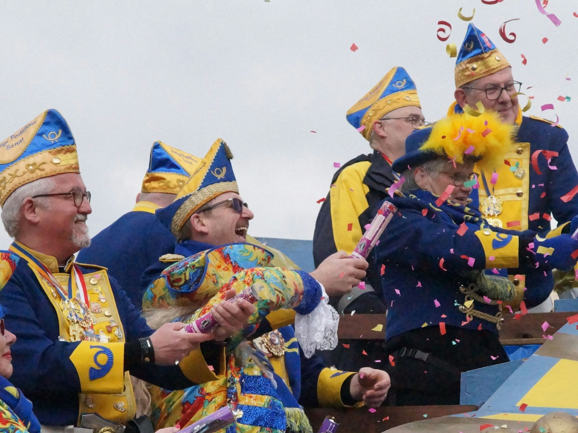 Eine Gruppe Karnevalisten auf einem blau-gelben Wagen im Wesselinger Zug wirft Konfetti und jubelt.