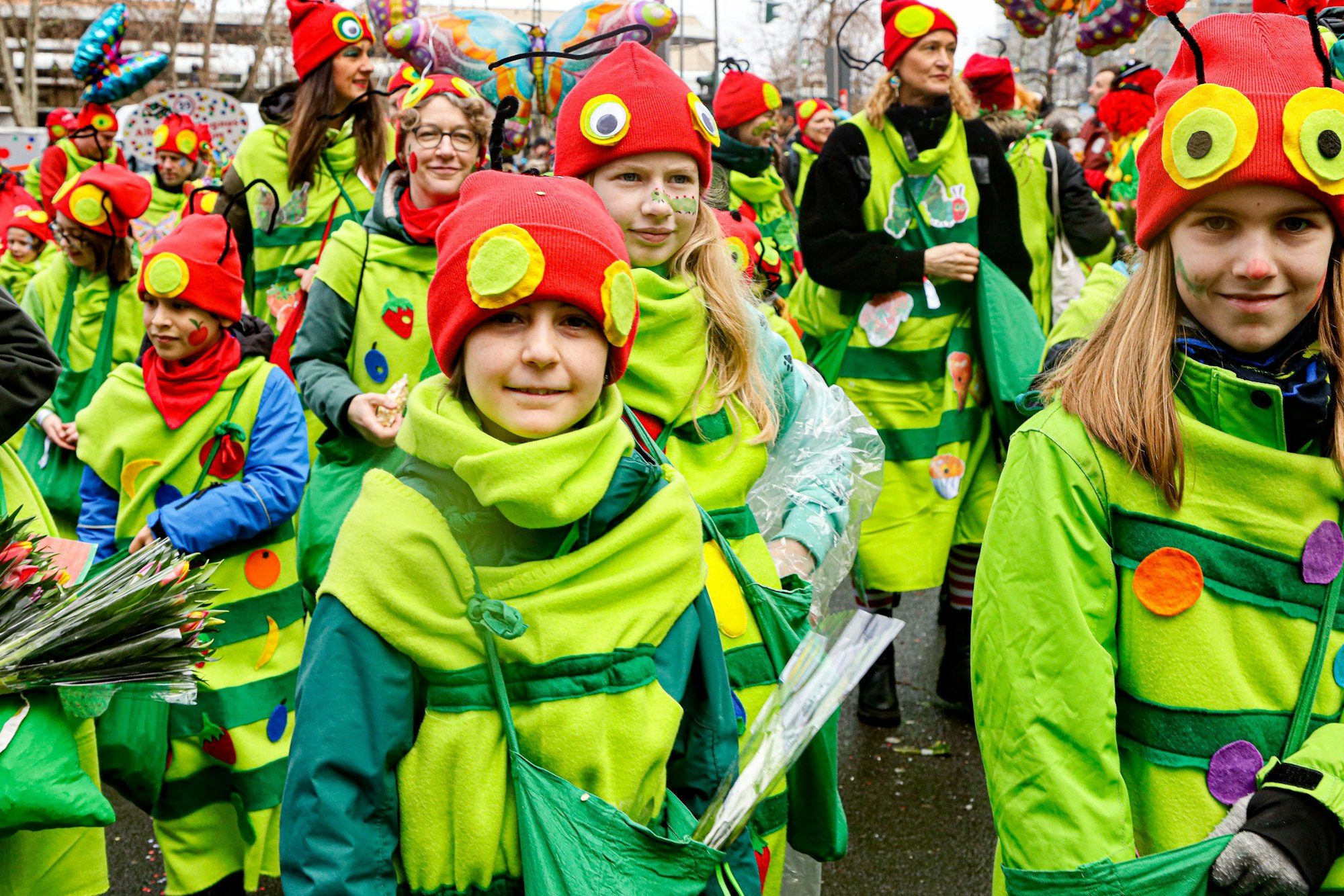 Schülerinnen und Schüler tragen grüne Kostüme mit roten Mützen.