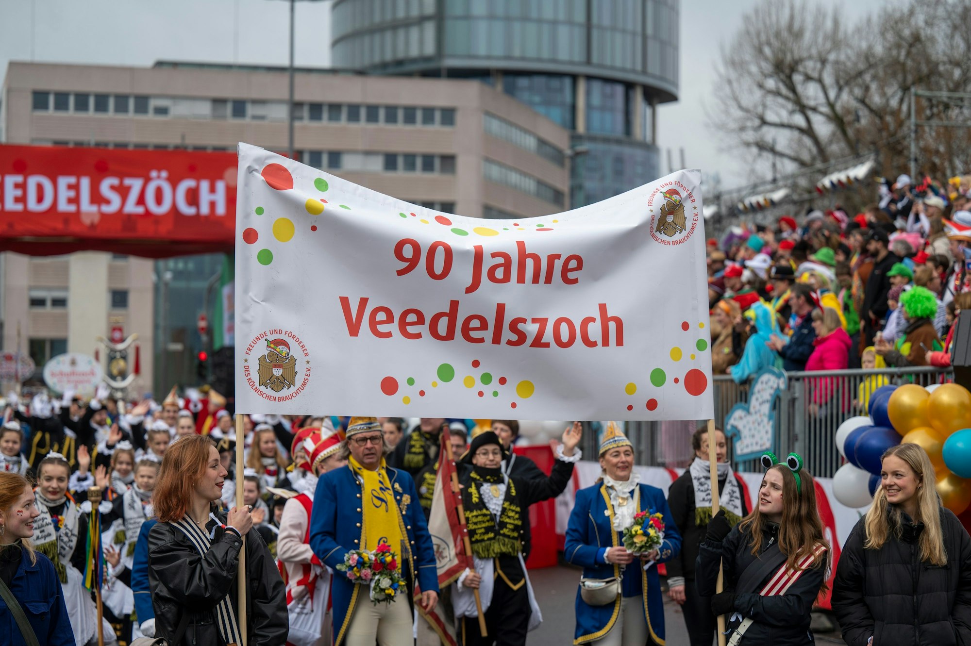Ein Banner mit der Aufschrift „90 Jahre Veedelszoch“ wird am Start in die Höhe gehalten.