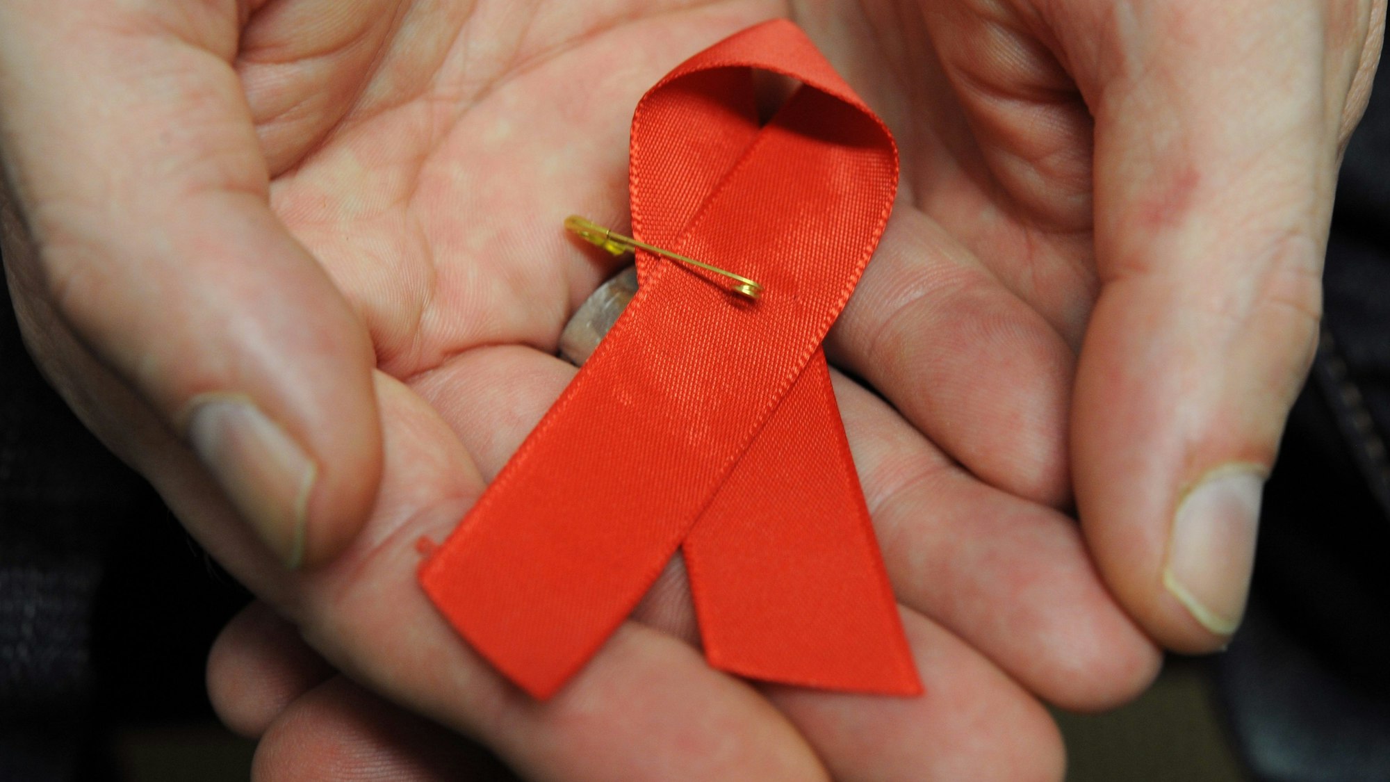 Ein mit dem HI-Virus infizierter Mann hält eine rote Schleife als Symbol der Solidarität mit HIV-Positiven und Aids-Kranken. (Symbolbild)
