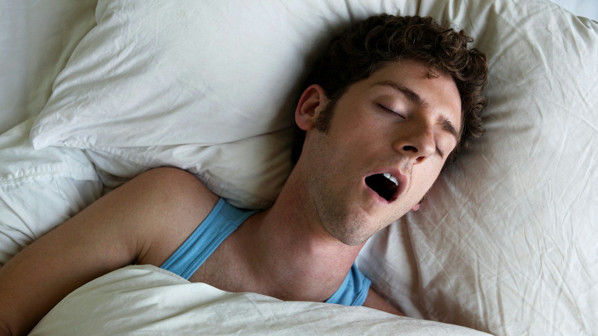 Mann liegt im Bett und schnarcht mit offenem Mund.