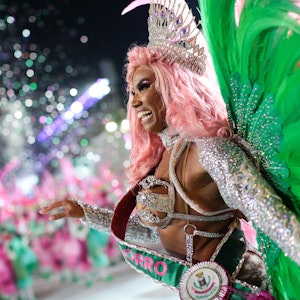 Das Symbolfoto aus dem Jahr 2022 zeigt eine Tänzerin beim Karneval in Rio de Janeiro. Sie trägt Flügel aus grünen Federn, hat rosafarbene Haare und viel Glitzer an ihrem Körper.