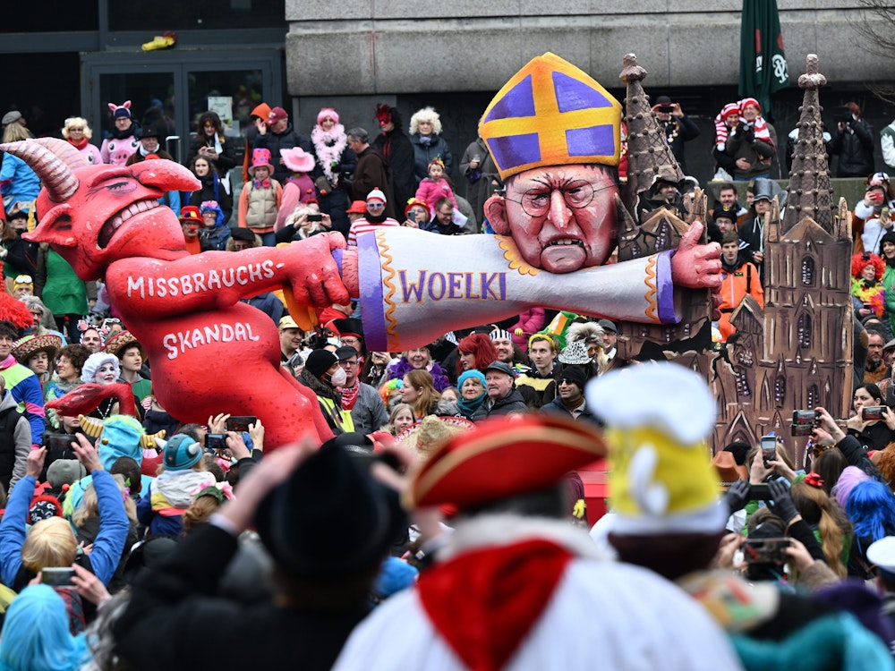 Ein Mottowagen zeigt den Teufel, der am Kölner Kardinal Woelki zerrt, der sich am Kölner Dom festklammert.