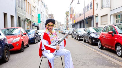 Die Mohrenstraße in Köln am Rosenmontag.Tobias Oentrup, verkleidet als Elvis Presley, sitzt auf einem Stuhl mitten auf der Straße