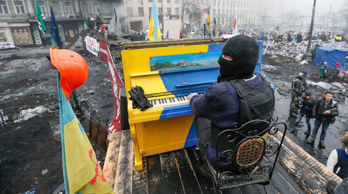 Ein am 22. November 2014 veröffentlichtes Bild aus dem Archiv zeigt einen ukrainischen Demonstranten, der während der anhaltenden Euromaidan-Proteste in Kyjiw auf einer Barrikade Klavier spielt. Das Klavier ist in den Nationalfarben der Ukraine gestrichen. Es liegen Trümmer drumherum.