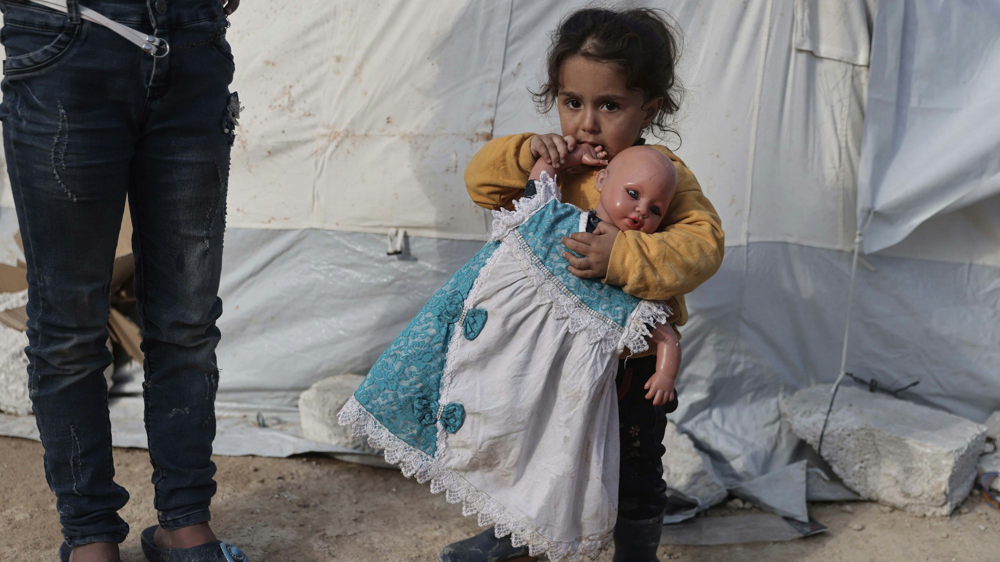 19.02.2023, Syrien, Salqin: Ein Kind hält eine Puppe in der Hand in einer Notunterkunft, die für die Opfer des Erdbebens an der türkisch-syrischen Grenze errichtet wurde. In Syrien sind bisher rund 5900 tote Menschen in Zusammenhang mit den verheerenden Beben gezählt worden.
