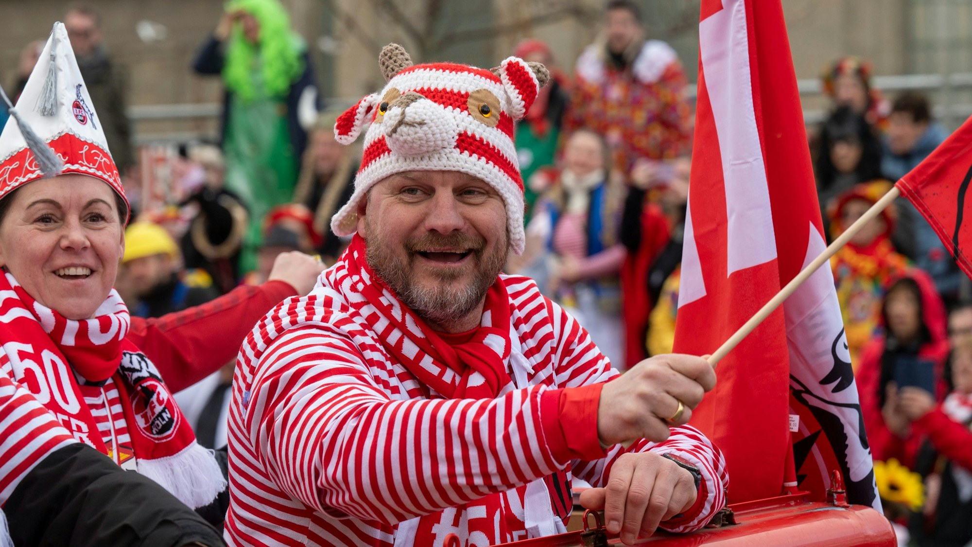Steffen Baumgart trägt Rot und Weiß und schwenkt lachend eine Fahne – und trägt dazu die Mütze, die er nach dem Spiel gegen Leipzig ertauscht hat. Mit ihm im Bild Nicole Bender, die Managerin der Kölner Frauenmannschaft