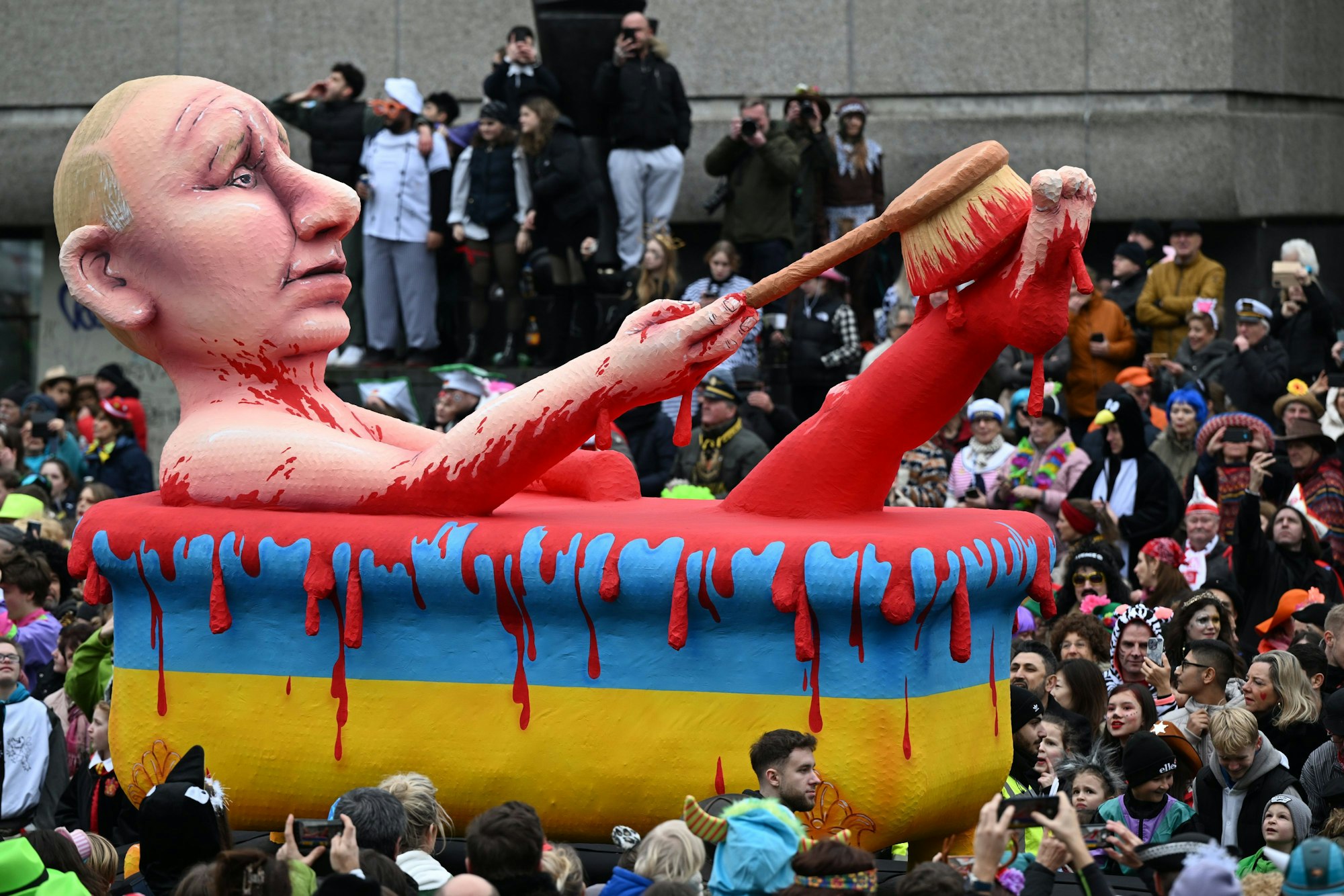 Putin sitzt in einer Badewanne in den ukrainischen Nationalfarben und schrubbt sich den Fuß mit einer Bürste, das Wasser ist rot wie Blut.