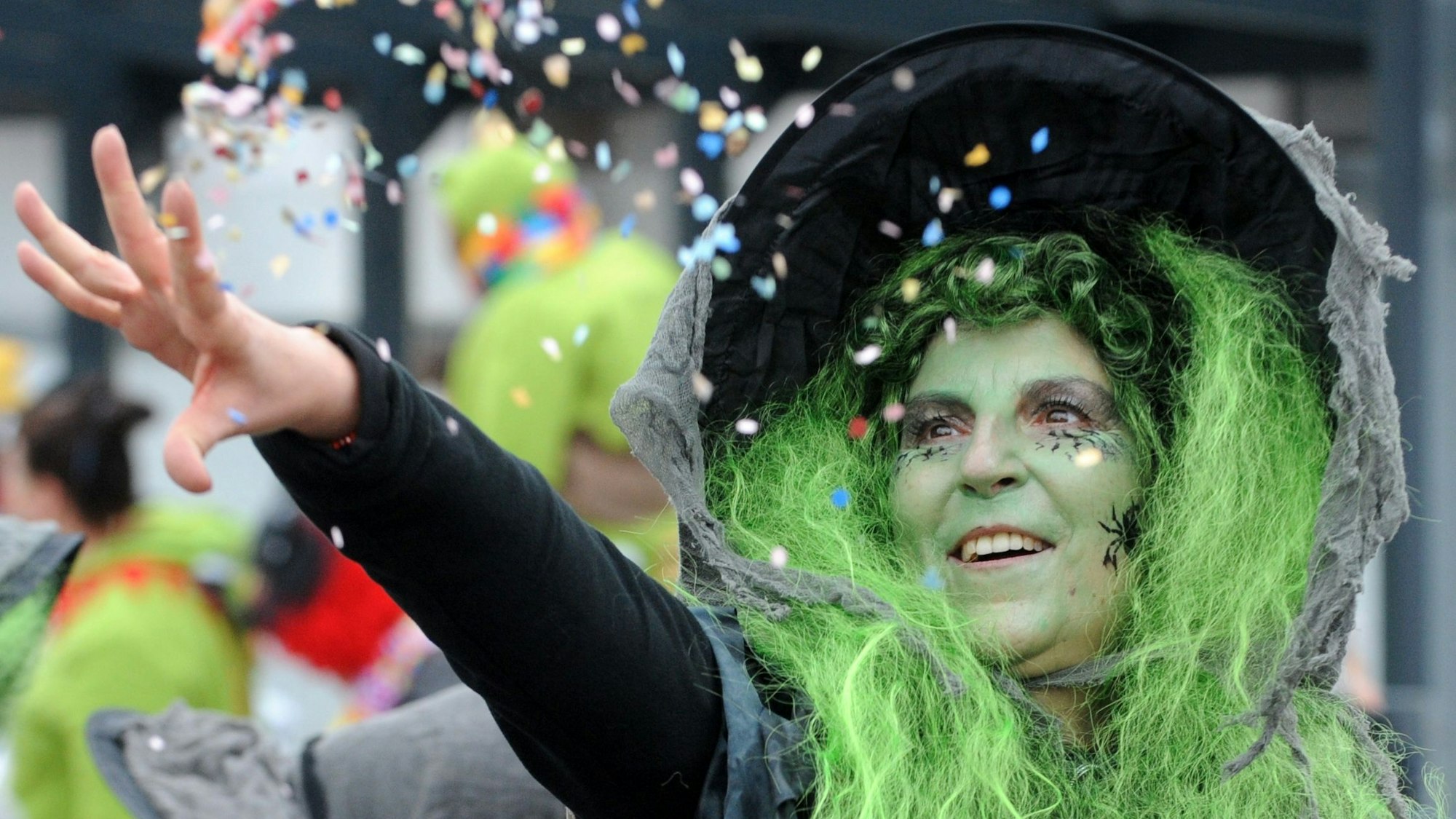 Eine Hexe mit grünen Haaren wirft mit Konfetti.