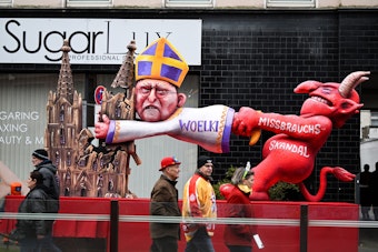 Ein Mottowagen befasst sich mit dem Missbrauchsskandal in der katholischen Kirche und zeigt den Teufel und den Kölner Kardinal Woelki.