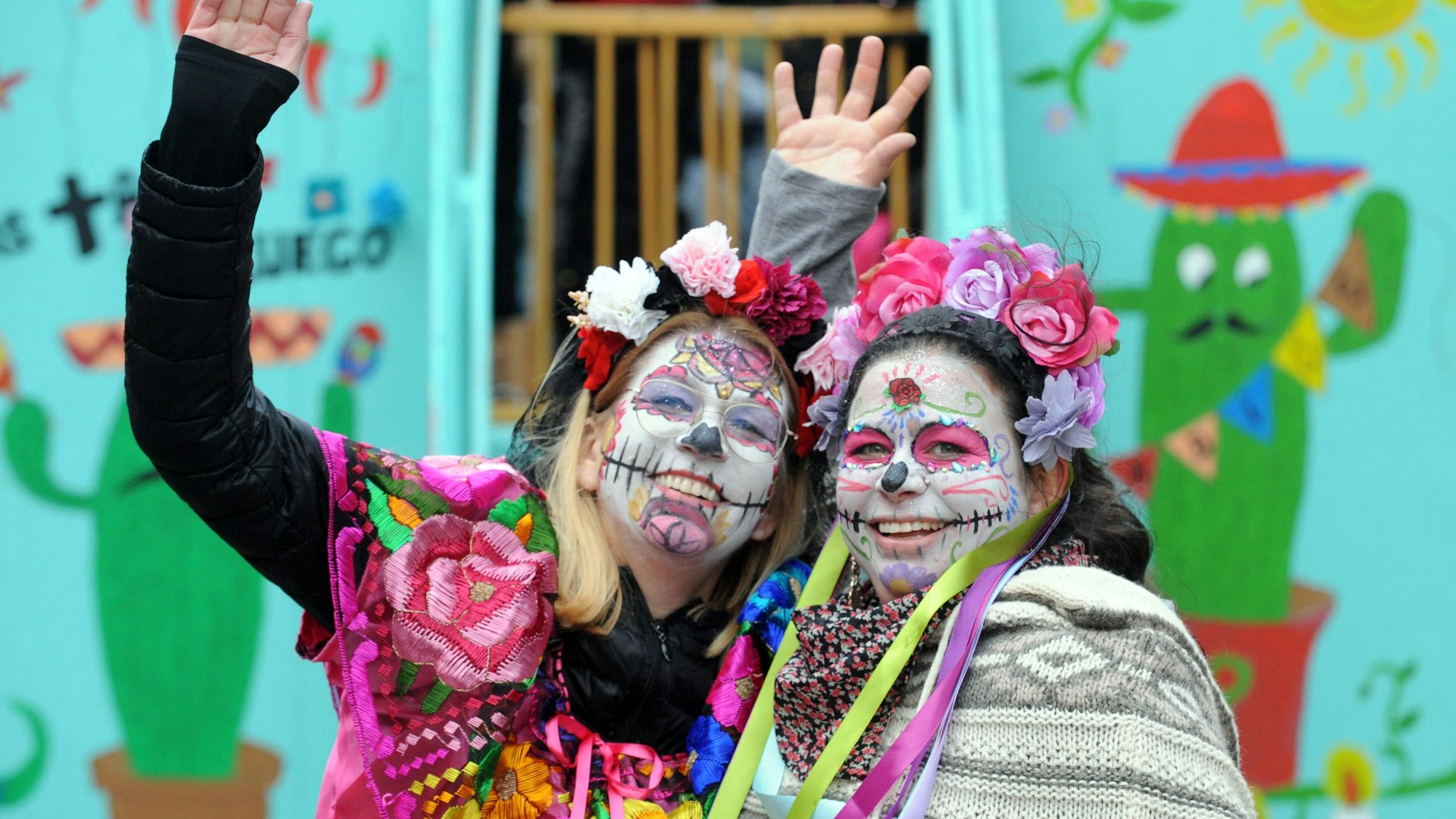 Zwei Frauen, verkleidet in einem farbenfrohen Dia de los Muertos Kostüm, lächeln in die Kamera.