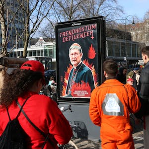 Plakataktion im Karneval: Jecke beobachten am Rosenmontag in Köln die Plakate, die sich gegen Kardinal Woelki und das Kölner Erzbistum richten.